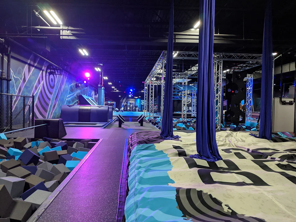 purple-lit walkway between the foam pits, with aerial silks overhead — the run kids get during a party slot